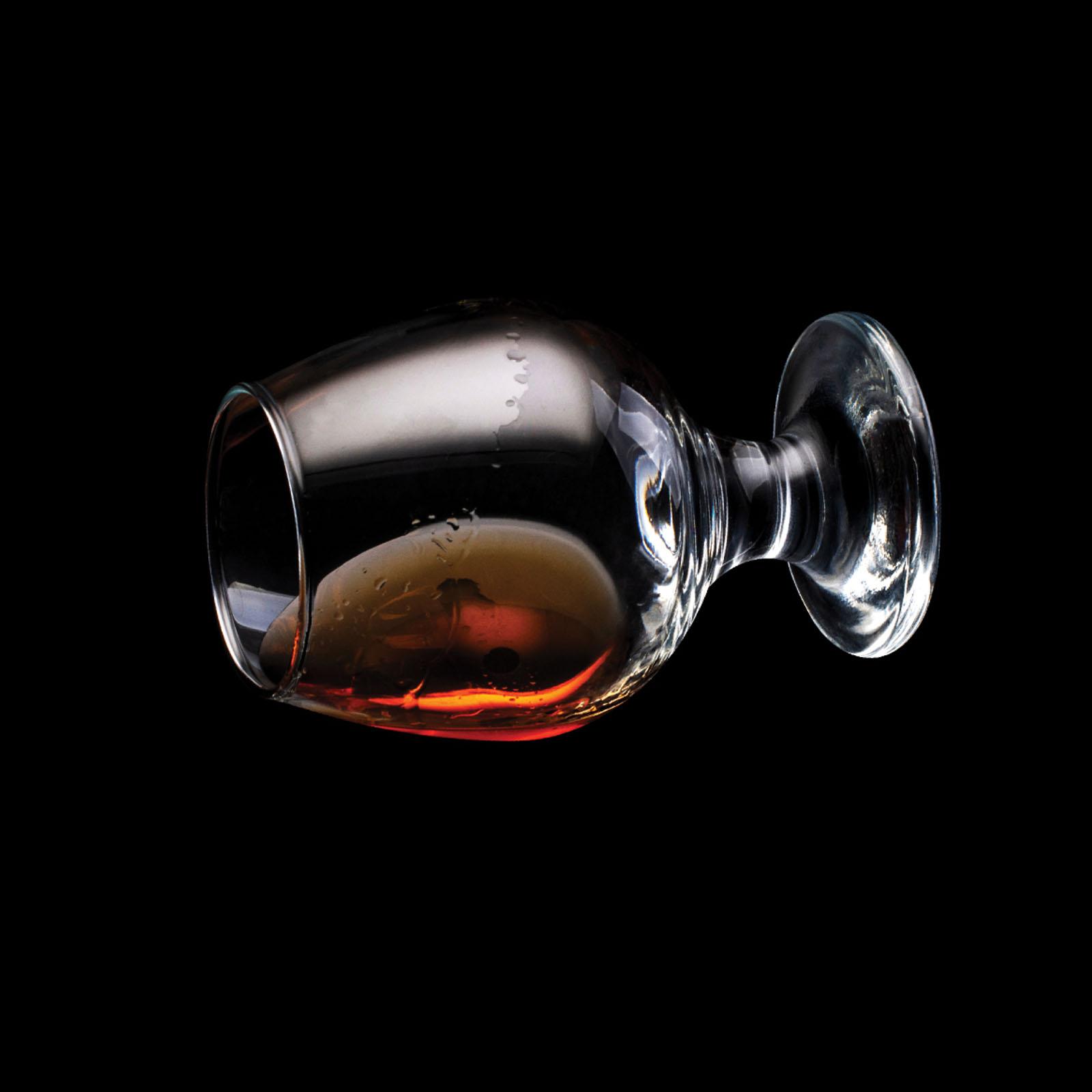 A glass of brandy on its side against a black background